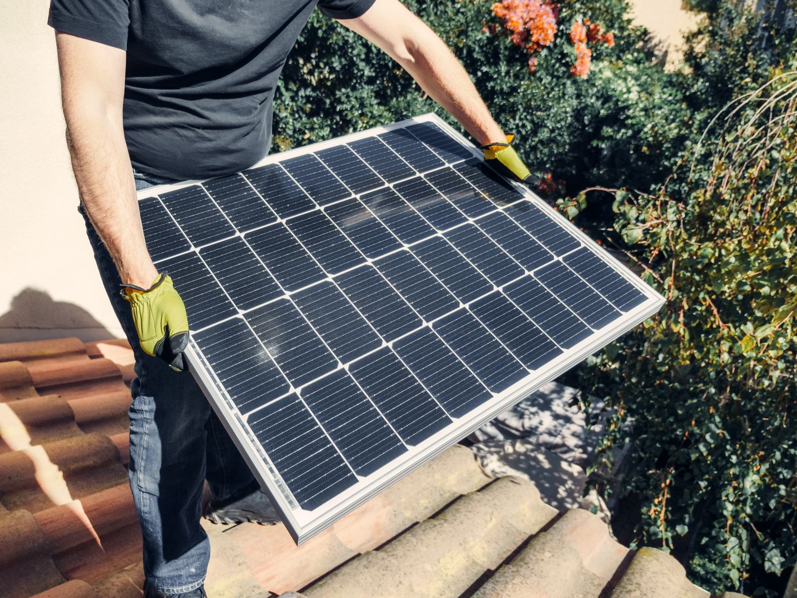 Installateur portant un panneau solaire sur un toit de tuiles